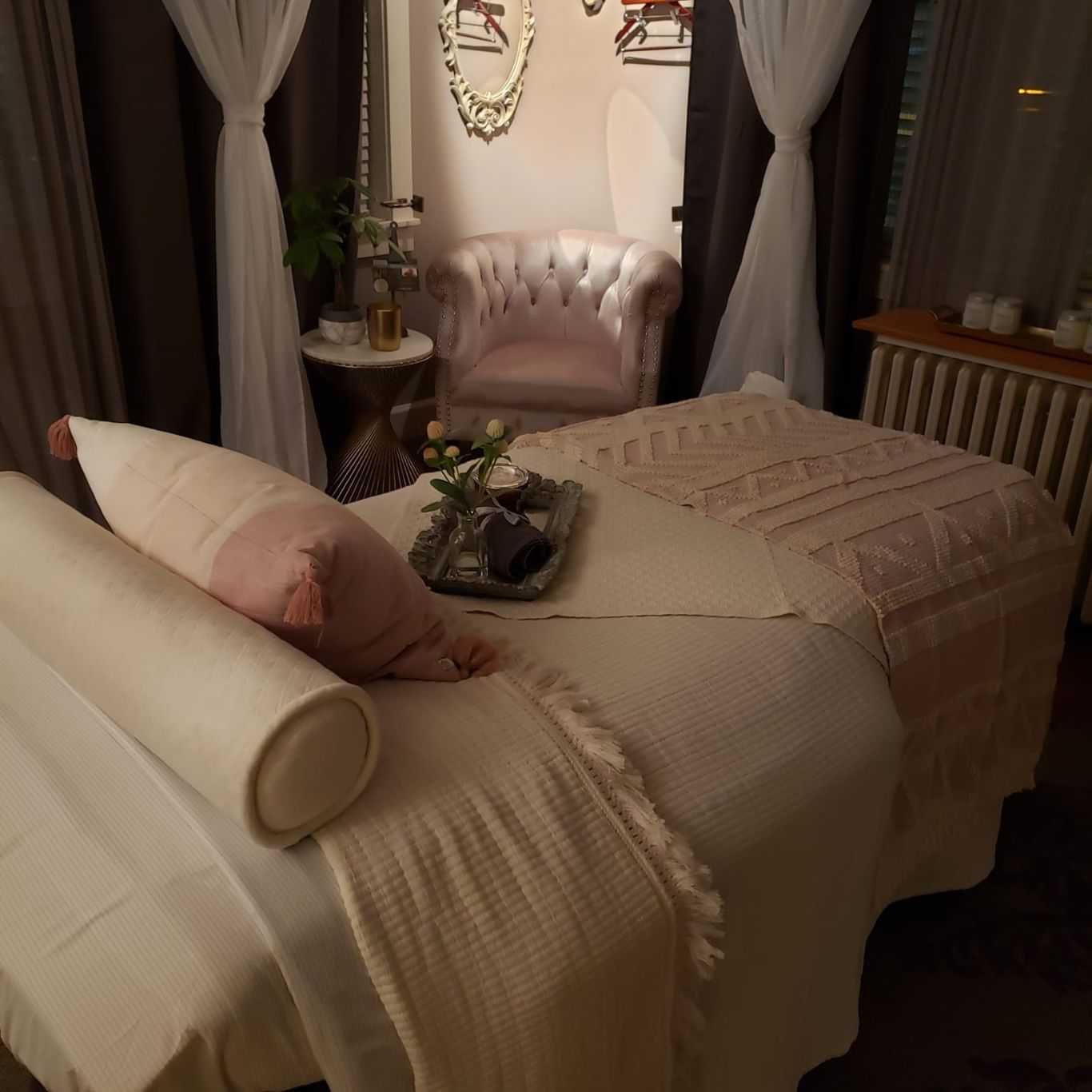 Spa room with a massage table, cozy chair, and soft lighting for a relaxing ambiance.