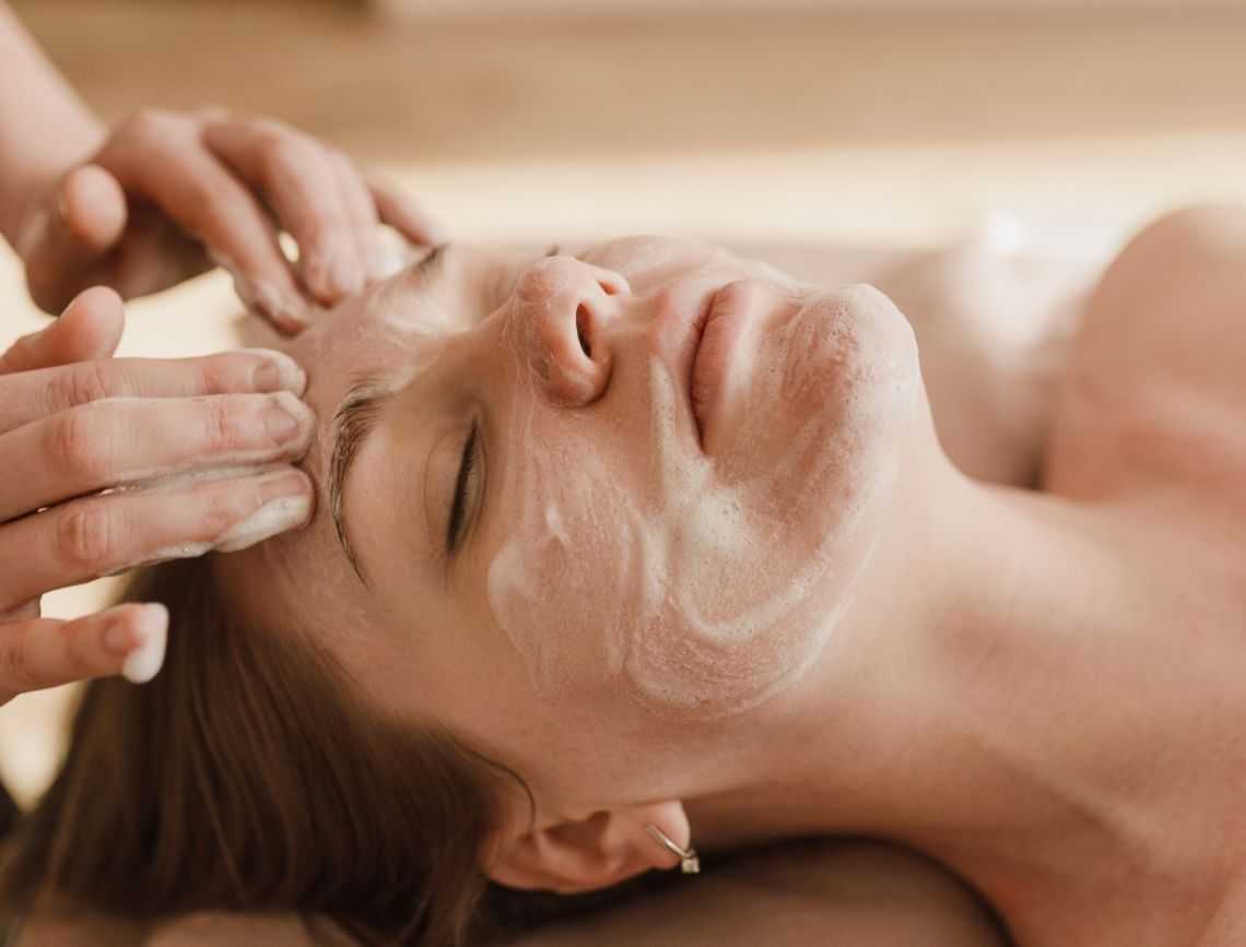 Woman receiving a relaxing facial massage with a cleansing cream on her face.
