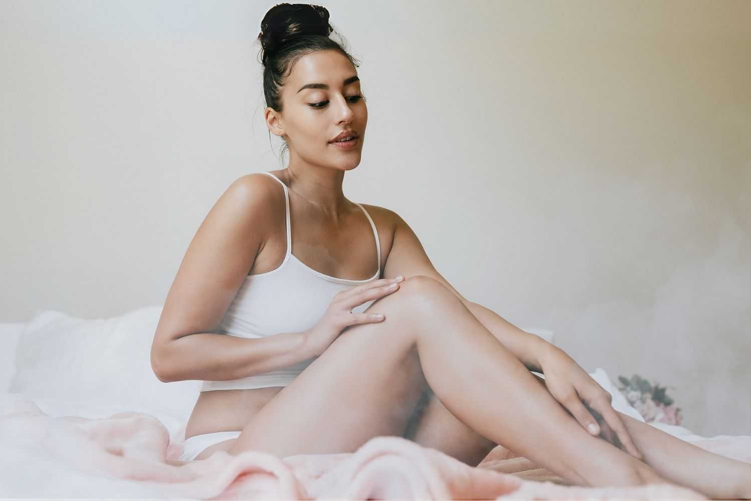 Woman in a white outfit sitting on a bed with a relaxed expression.
