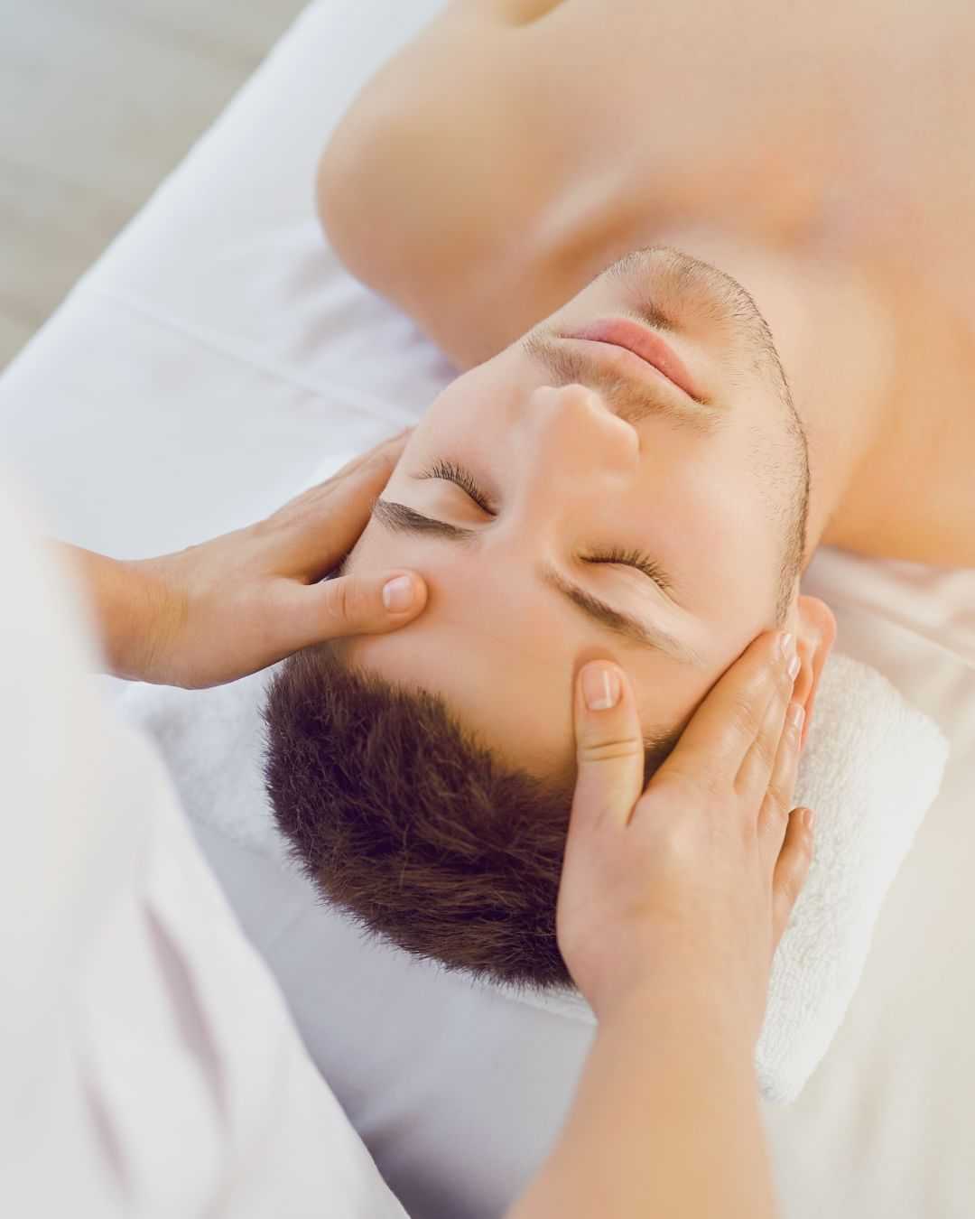 Person receiving a relaxing facial massage with closed eyes, lying on a white towel.